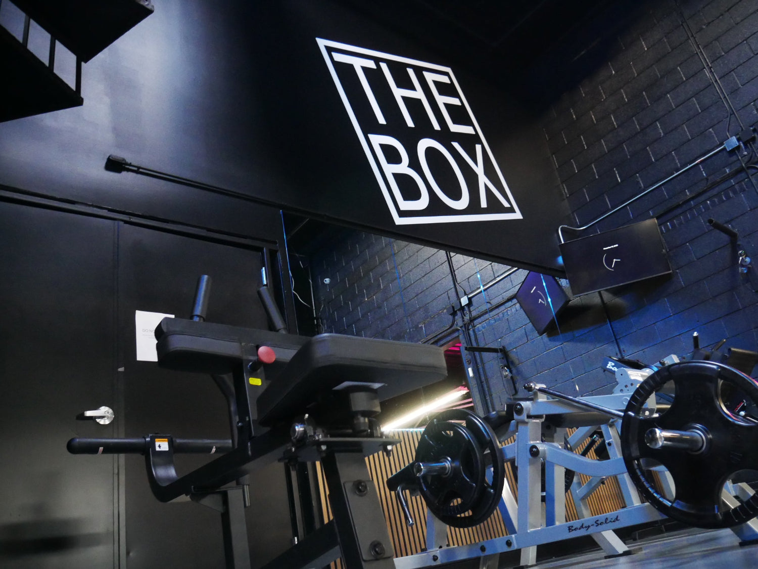 Gym interior with exercise equipment and 'The Box' branding on a black wall.