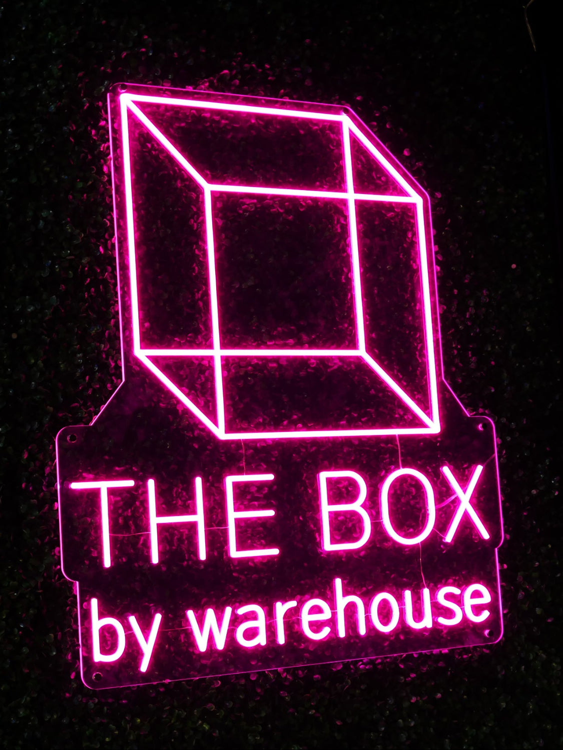 Neon sign of a cube with 'The Box by Warehouse' text on a black background